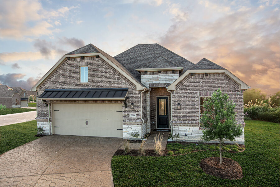 Brick single-story Ladera home with two-car garage, landscaped yard, and sunset sky in the background