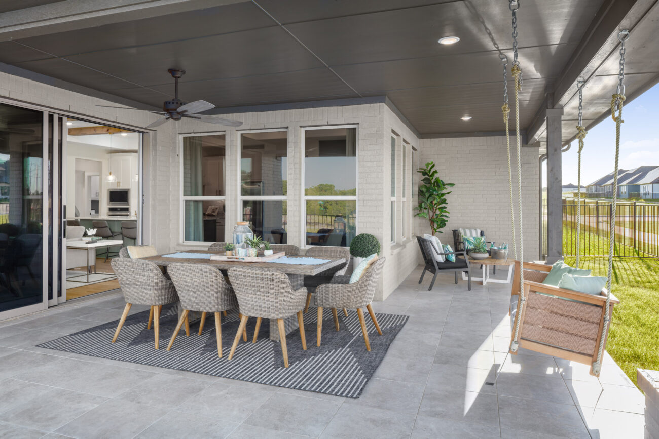 Spacious covered patio with dining set, ceiling fan, swing bench, and lounge chairs overlooking a fenced backyard and neighborhood