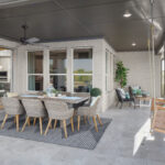 Spacious covered patio with dining set, ceiling fan, swing bench, and lounge chairs overlooking a fenced backyard and neighborhood
