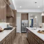 Modern kitchen with stainless steel appliances, pendant lights, wood cabinets, gas cooktop, and spacious quartz countertops