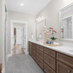 Modern bathroom at Ladera Living featuring dual sinks, natural wood cabinetry, and sleek decor with neutral tile and finishes