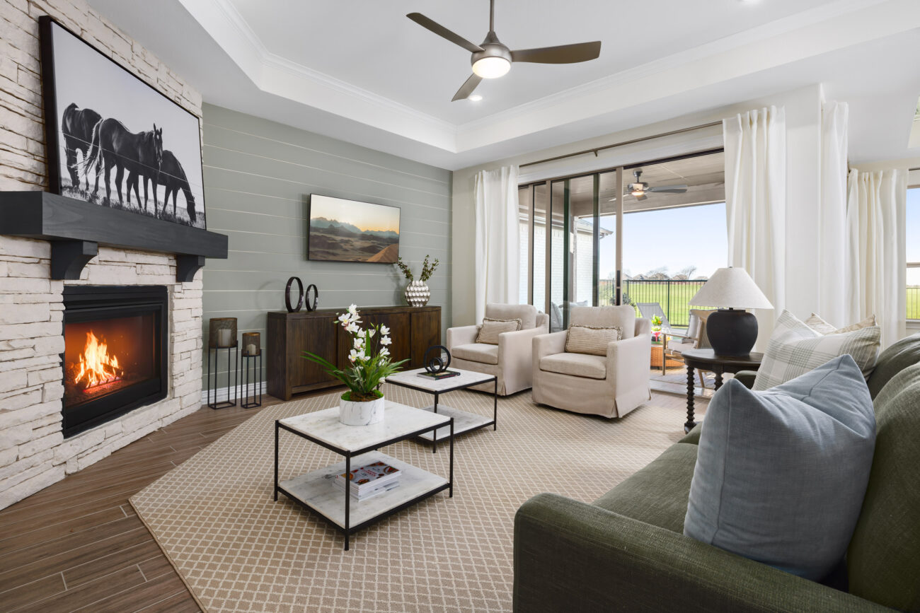Living room with stone fireplace, green sofa, two armchairs, and sliding glass doors to a covered patio