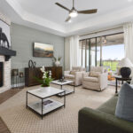 Living room with stone fireplace, green sofa, two armchairs, and sliding glass doors to a covered patio