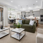 Open-concept living room with green sofa and marble coffee tables, opening to a modern kitchen and patio doors