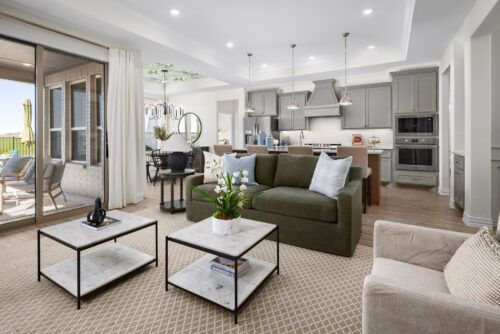 Open-concept living room with green sofa and marble coffee tables, opening to a modern kitchen and patio doors