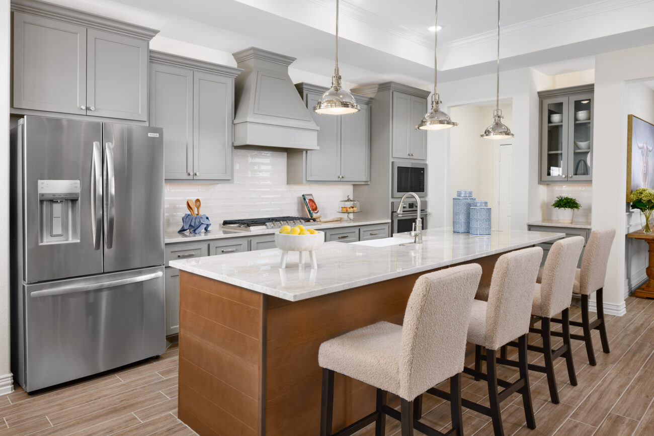 Modern kitchen with large quartz island, five bar stools, gray cabinets, stainless fridge, and pendant lights