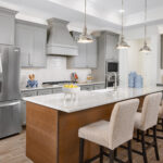 Modern kitchen with large quartz island, five bar stools, gray cabinets, stainless fridge, and pendant lights