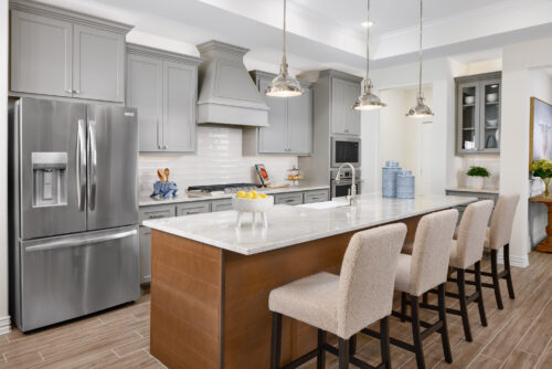 Modern kitchen with large quartz island, five bar stools, gray cabinets, stainless fridge, and pendant lights