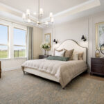 Staged primary bedroom with upholstered bed, large rug, modern chandelier, and two windows with curtains