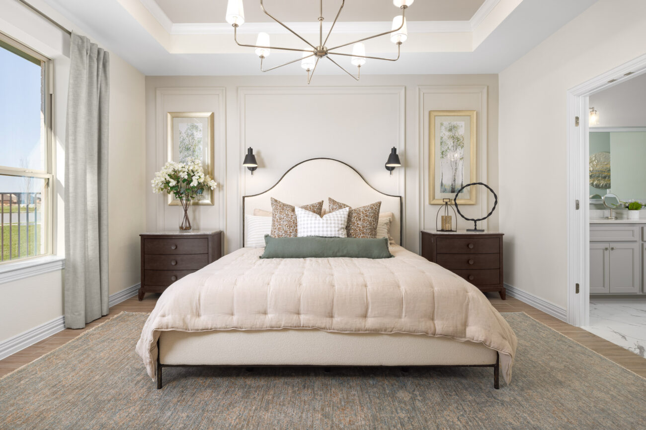 Bright primary bedroom with upholstered bed, tray ceiling, and modern chandelier in a Ladera Living home