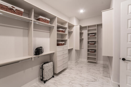 Spacious walk-in closet with built-in shelves and drawers, marble-style floor, and suitcase on wheels