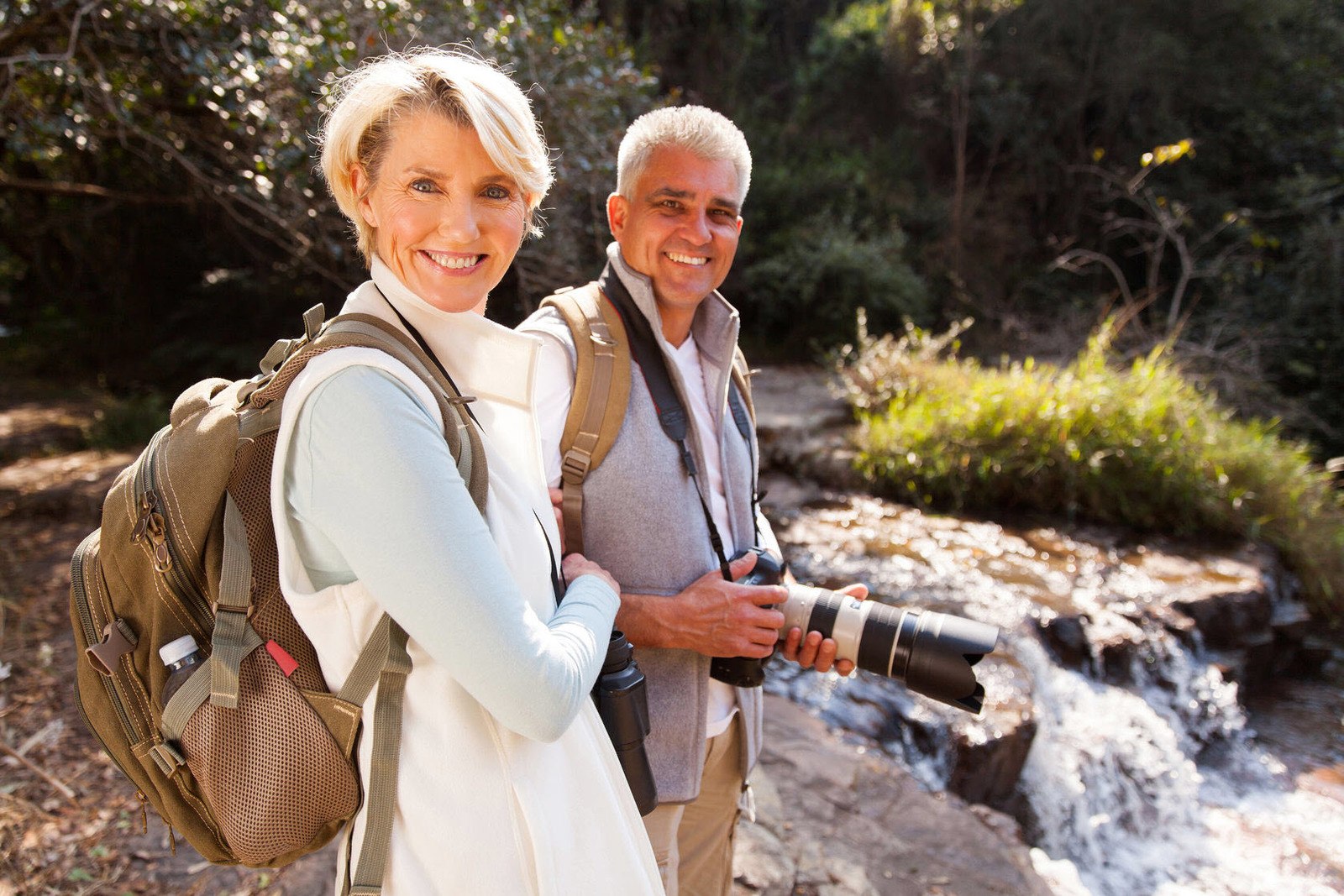 an-old-happy-couple-standing-near-the-falls-while-holding-a-camera.