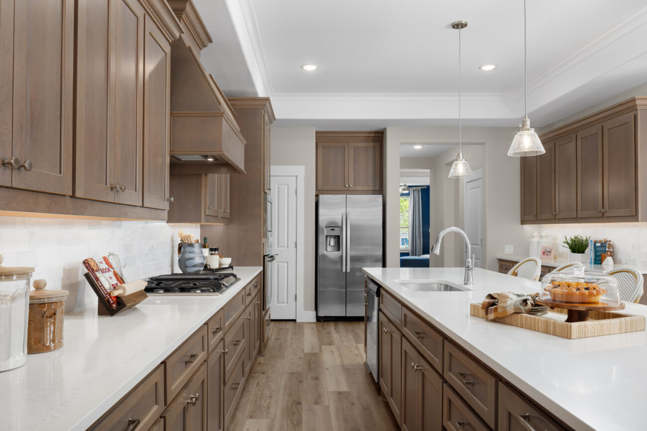 Modern kitchen with stainless steel appliances, pendant lights, wood cabinets, gas cooktop, and spacious quartz countertops