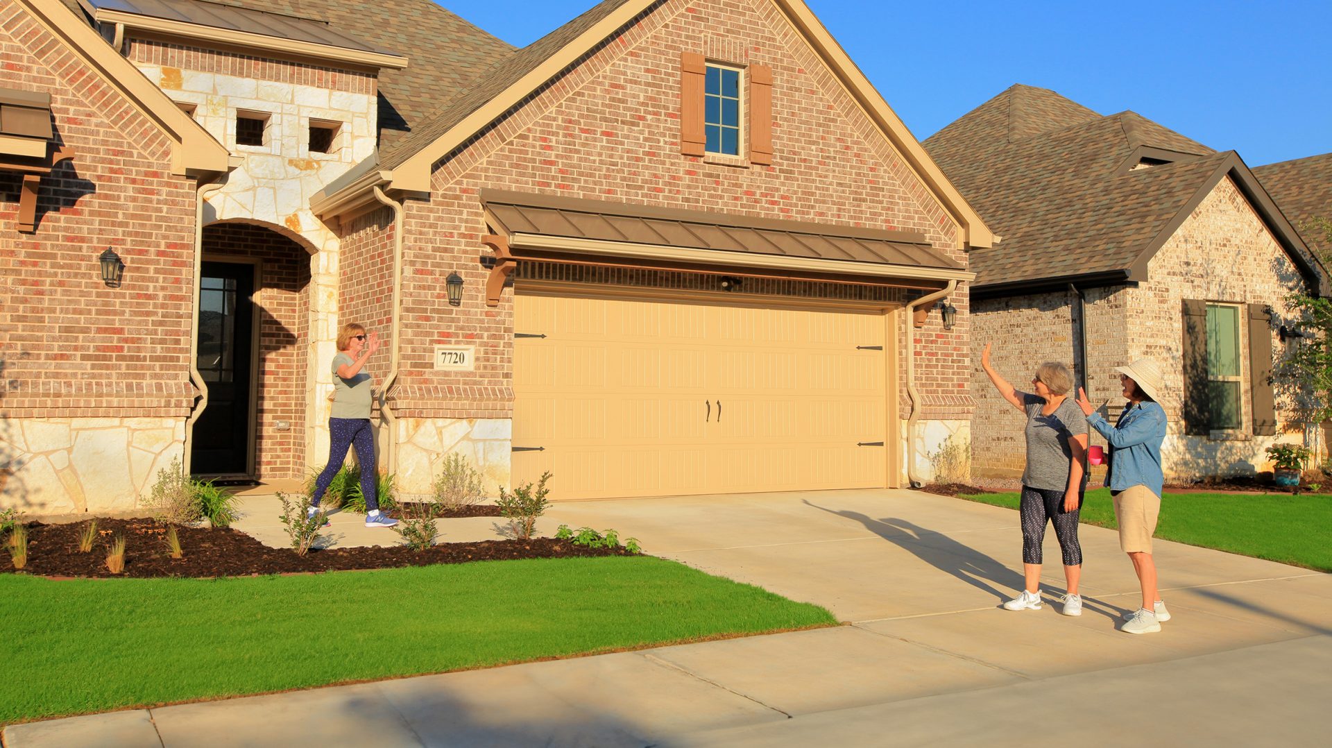 2 women waving to a woman outside her home