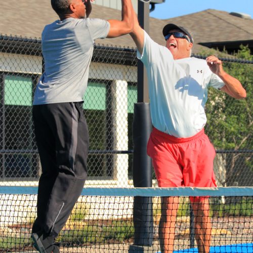 two men jumping tapping pickleball rackets