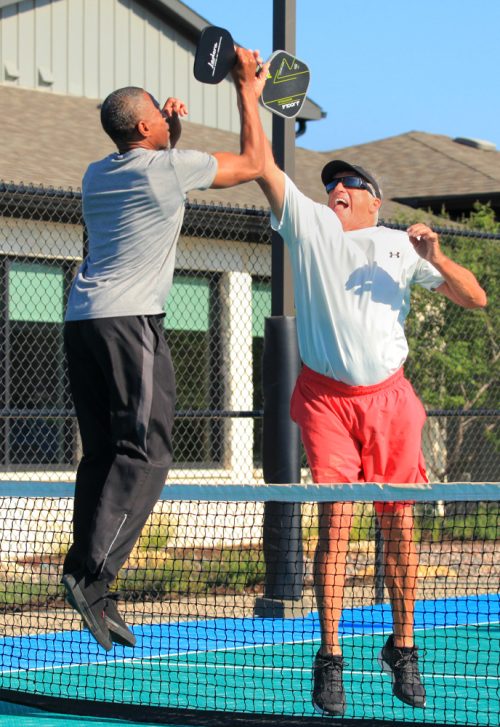 two men jumping tapping pickleball rackets