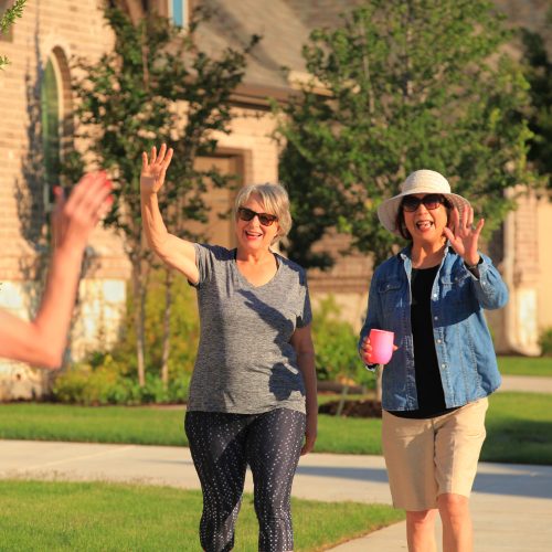 women walking and waving to a neighbor