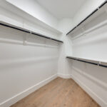 Spacious walk-in closet at Ladera Living with white shelving, hanging rods on three sides, and wood-style flooring