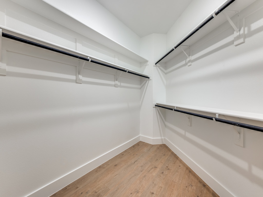 Spacious walk-in closet at Ladera Living with white shelving, hanging rods on three sides, and wood-style flooring