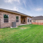Fenced backyard with green lawn and brick exterior home at Ladera Living, featuring a covered patio and private outdoor space