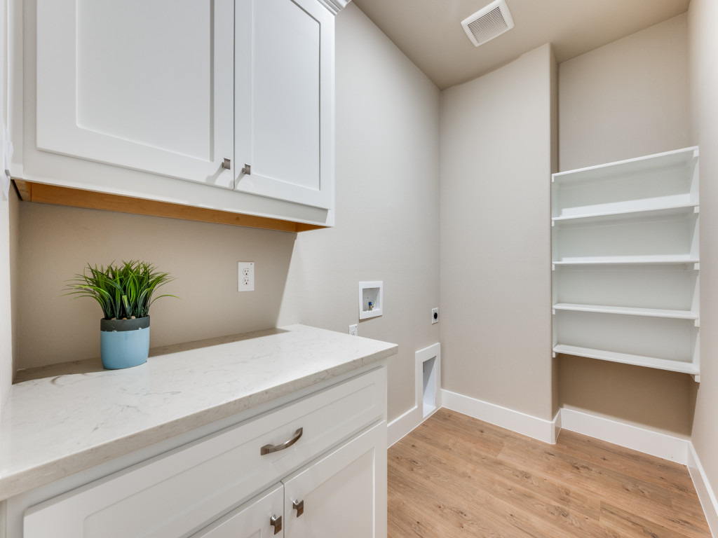 Bright utility room at Ladera Living with white cabinetry, built-in shelving, laundry hookups, and wood-style flooring