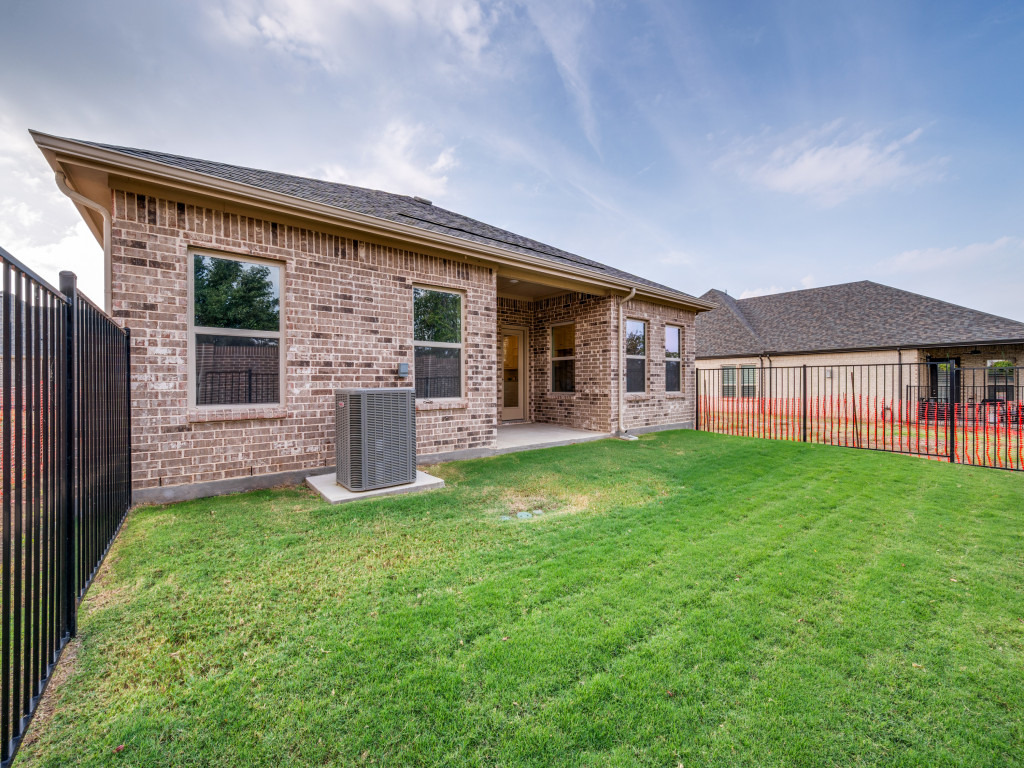 Fenced backyard with green lawn and brick exterior home at Ladera Living, featuring a covered patio and private outdoor space