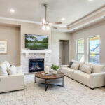 Bright, modern living room with white sofas, a stone fireplace, ceiling fan, and large windows in a Ladera Living home