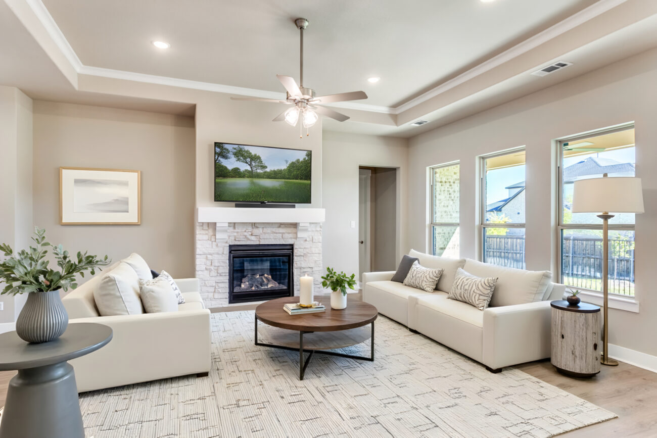 Bright, modern living room with white sofas, a stone fireplace, ceiling fan, and large windows in a Ladera Living home