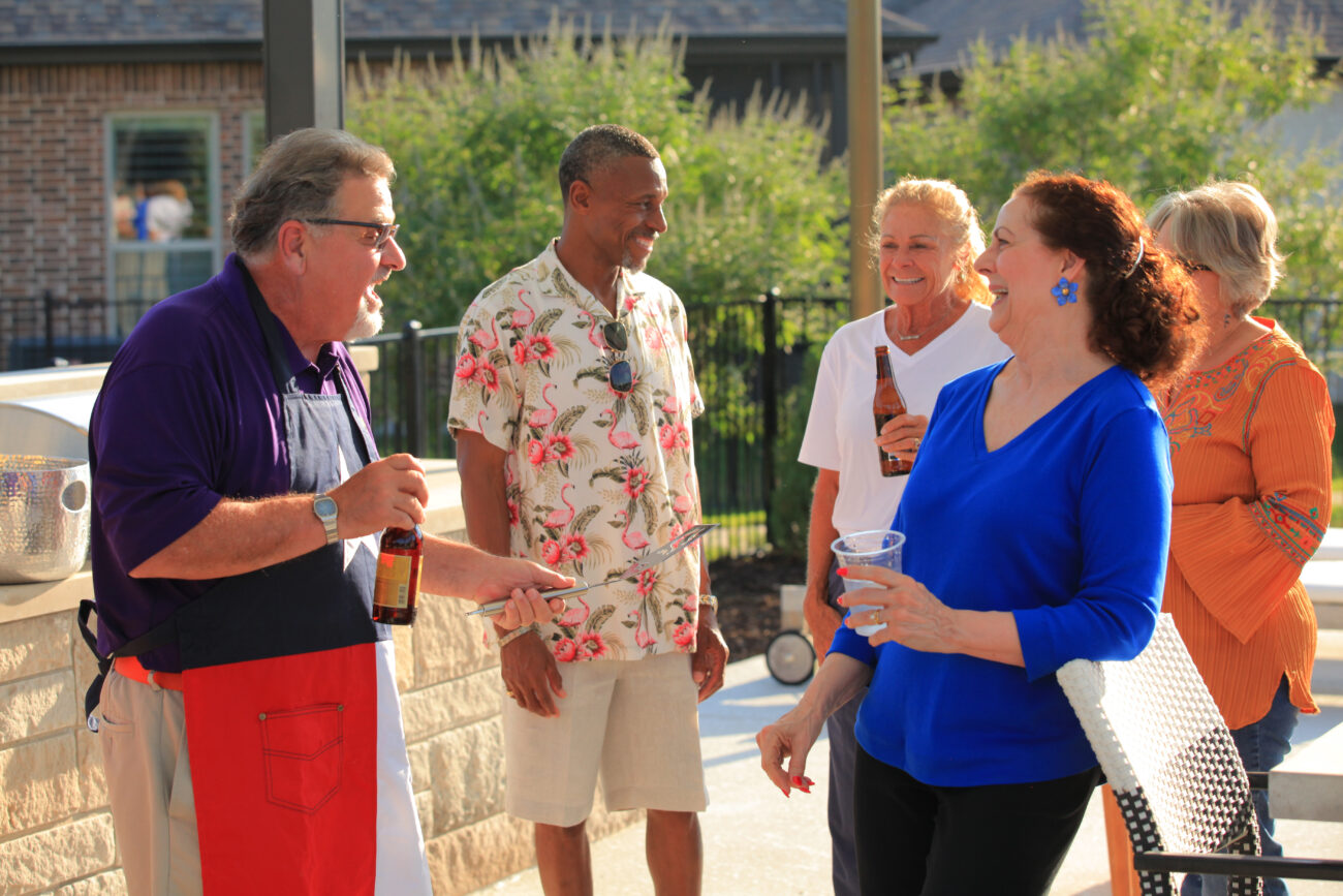 Group of 55+ active adults talking near a BBQ grill at The HUB amenity center in a Ladera Living 55+ community. Rightsizing seminars are coming this March